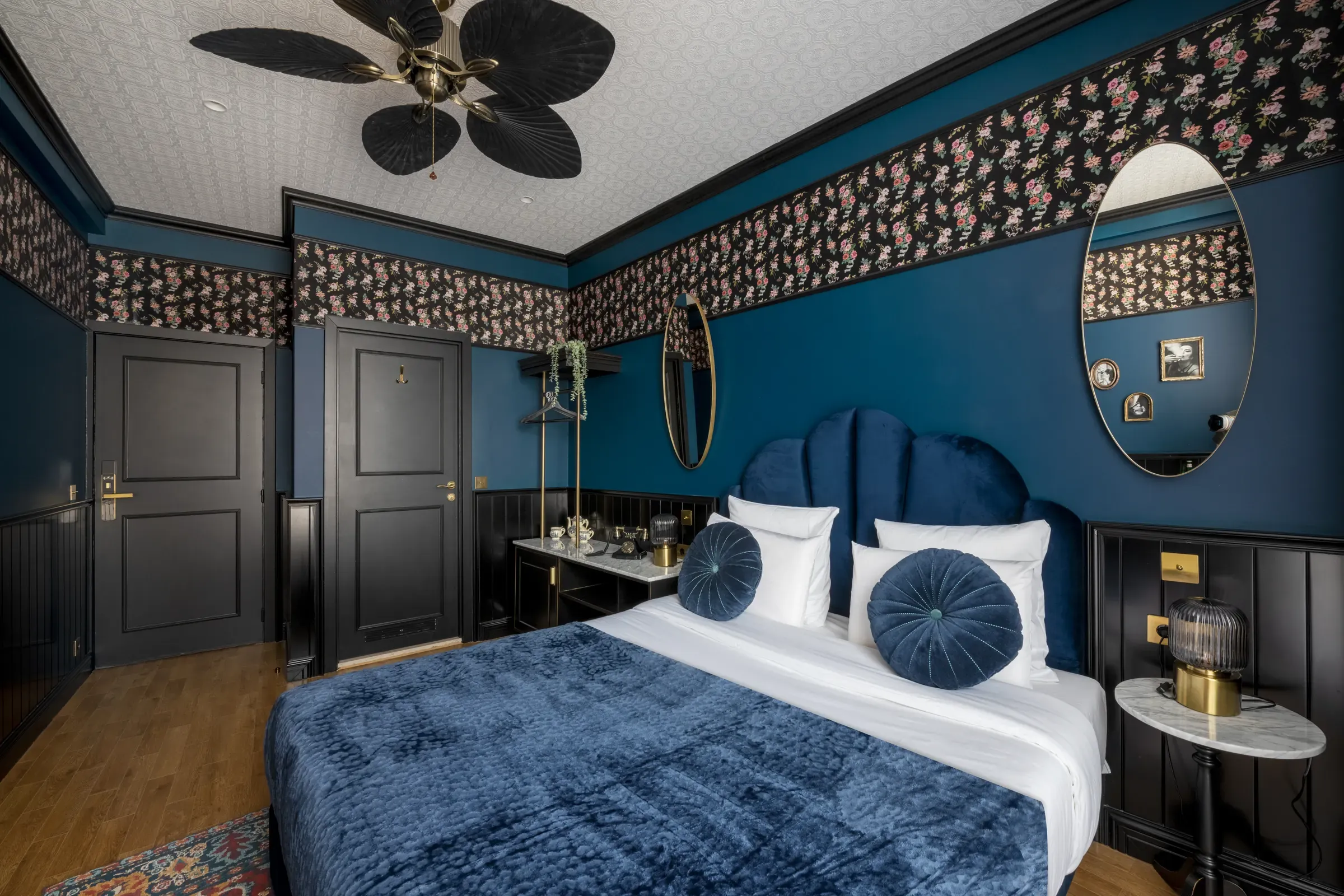 Chambre du Craves Hotel avec papier peint floral, tête de lit en velours bleu et ventilateur au plafond